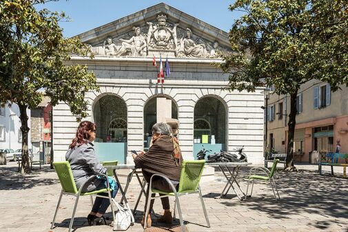 Deux personnes assises sur une chaise devant le bâtiment de la mairie de quartier du Centre et du Laurier